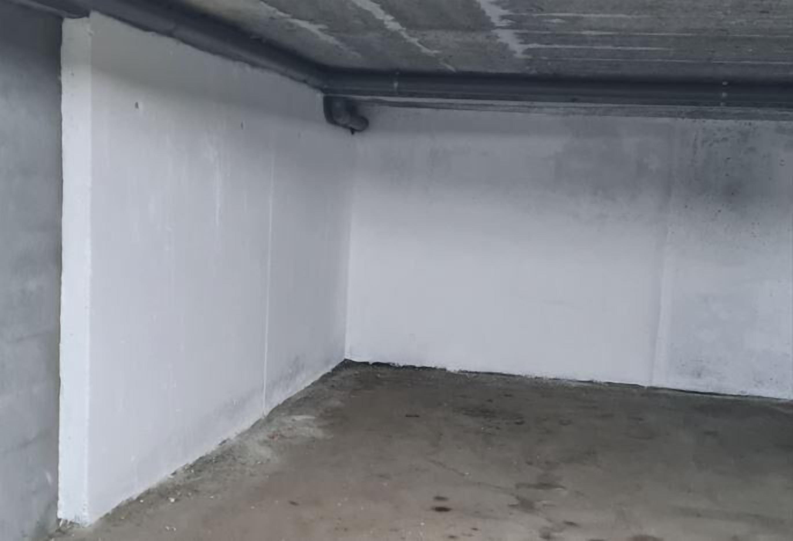 Una habitación con paredes blancas y suelo de concreto, que presenta un tubo a la vista en el techo.