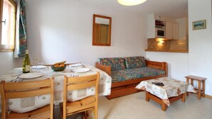 Una sala acogedora con una mesa de comedor preparada para dos personas, un sofá y una mesita con un control remoto.