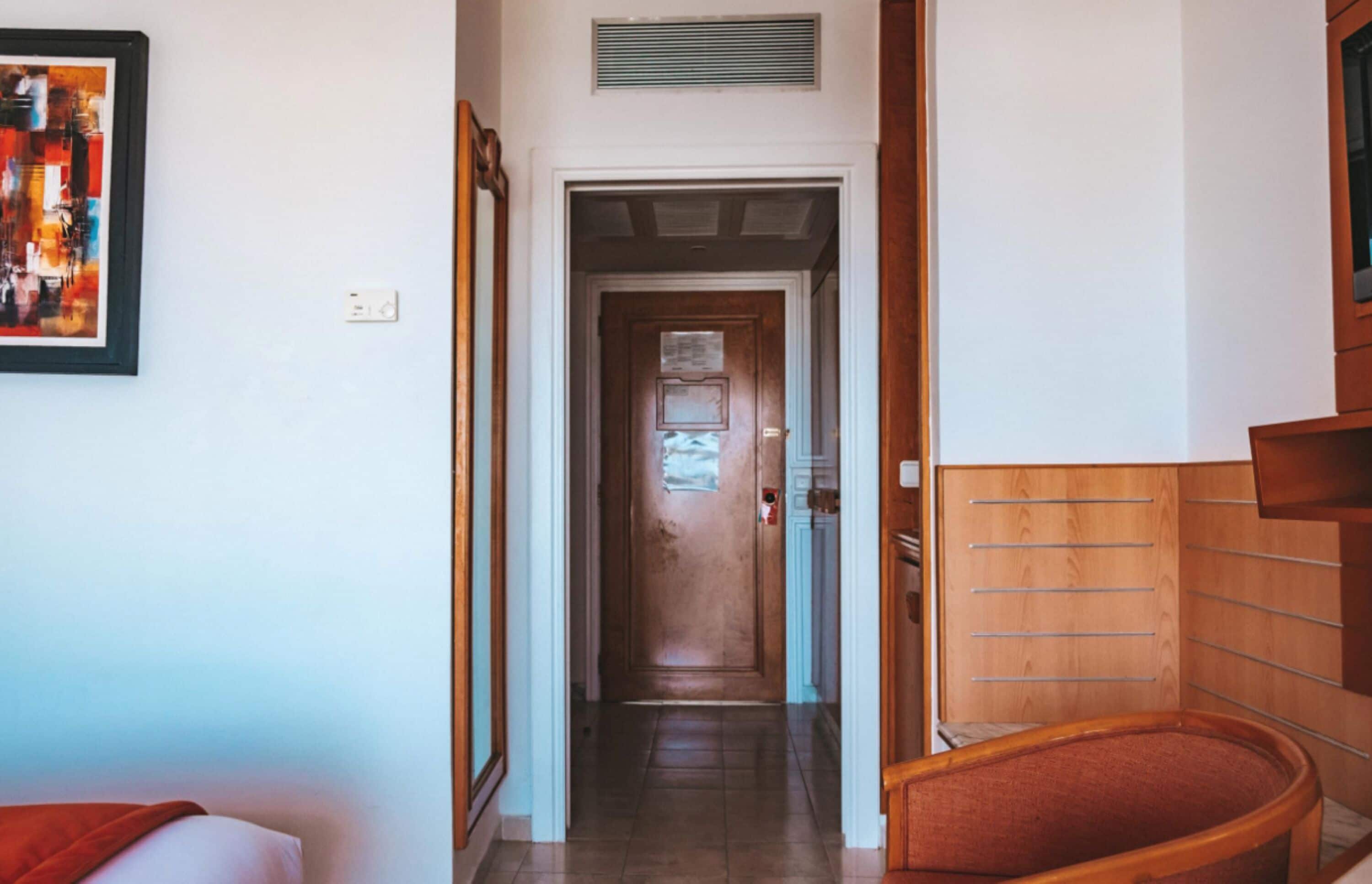 A hallway with a wooden door at the end, a framed artwork on the wall, and a wooden bench.