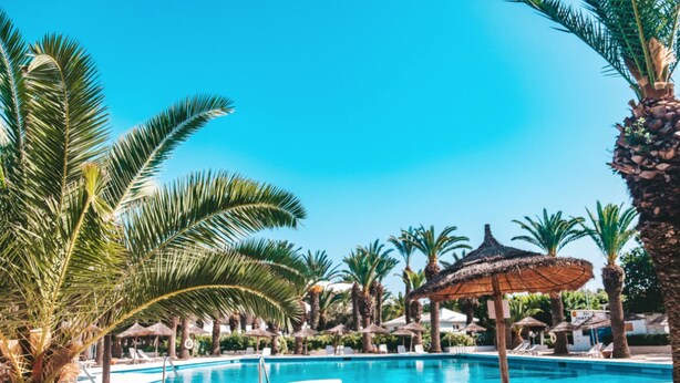 A clear blue sky, a swimming pool surrounded by palm trees, and thatched umbrellas. - Hotel Kanta Resort & Spa (Port El Kantaoui)