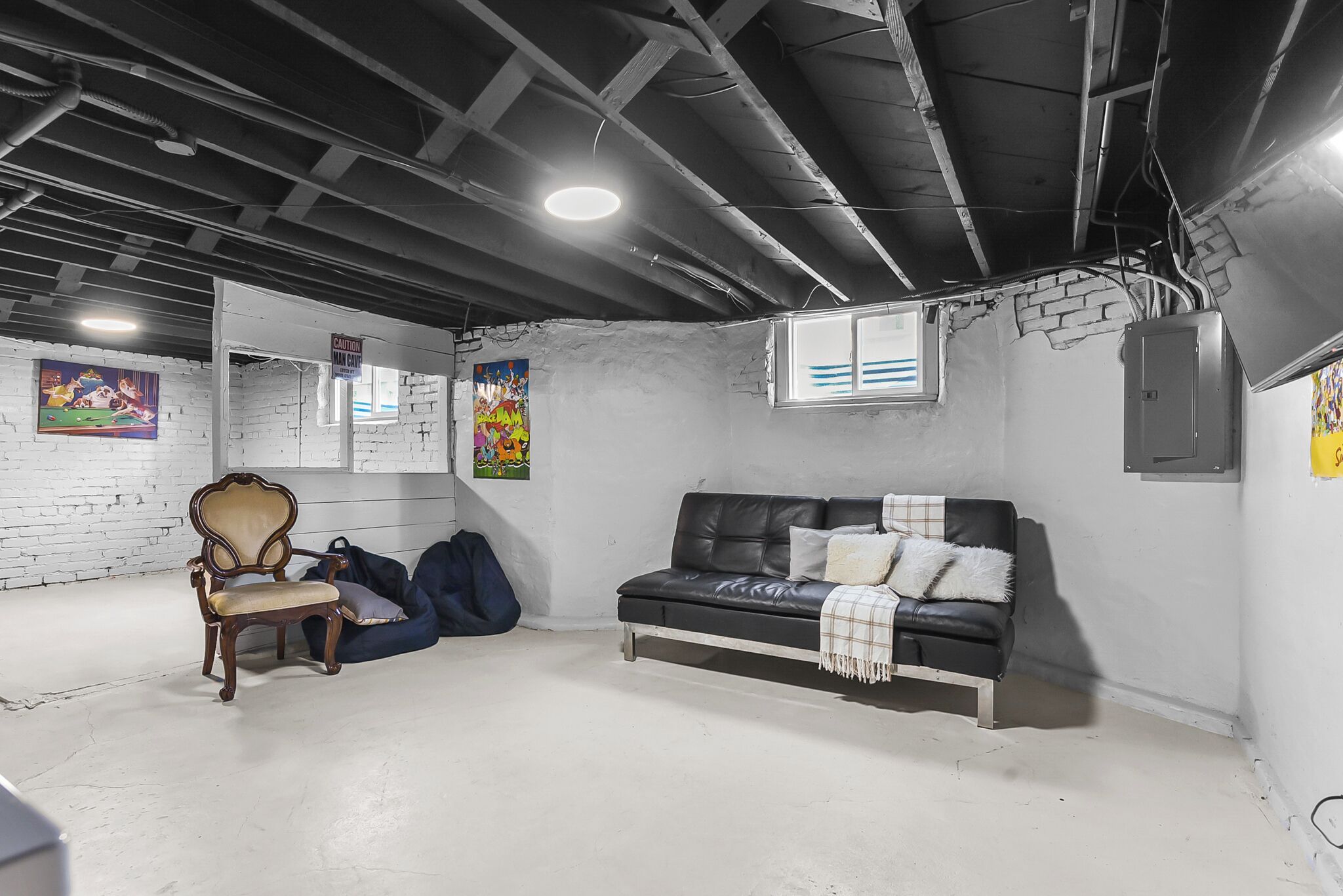 Relax in your private basement lounge with comfy seating, exposed beam charm, and vibrant wall art creating the perfect cozy retreat.