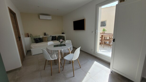 Une pièce moderne et bien éclairée, comprenant un lit, une table à manger avec des chaises et une porte-fenêtre coulissante donnant sur un espace extérieur.