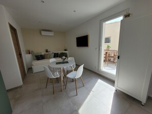 A modern, well-lit room with a bed, a dining table with chairs, and a sliding glass door leading to an outdoor area. - Cozy new 2-room apartment with a terrace, just 10 minutes from the ocean! (Châteauneuf-les-Martigues)
