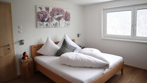 Una camera da letto con un letto di legno, biancheria bianca, un cuscino decorativo con un motivo cervo e un quadro di fiori appeso al muro.