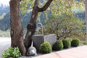 A stone fountain with a metal spout, surrounded by neatly trimmed bushes and a small hedgehog statue. - Ruhige Ferienwohnung in den Tiroler Bergen (Fließ)