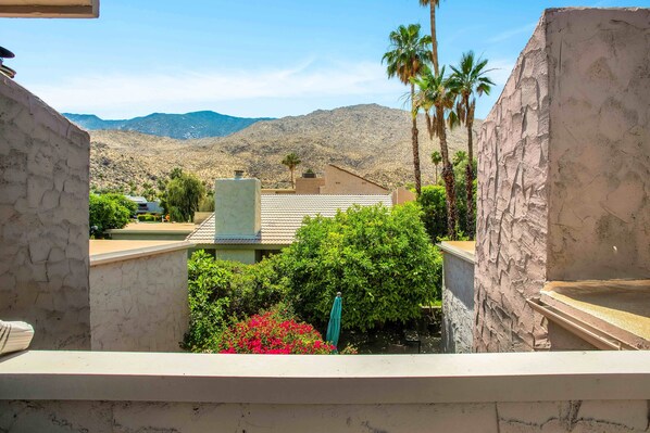 A view from a balcony overlooking a mountainous landscape with a house in the foreground, surrounded by greenery and palm trees. - Eclectic & Comfortable Canyon Corridor - A Ryson Property (Palm Springs)