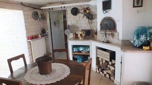 A rustic kitchen with a wooden table, chairs, a fireplace, and various kitchen utensils.