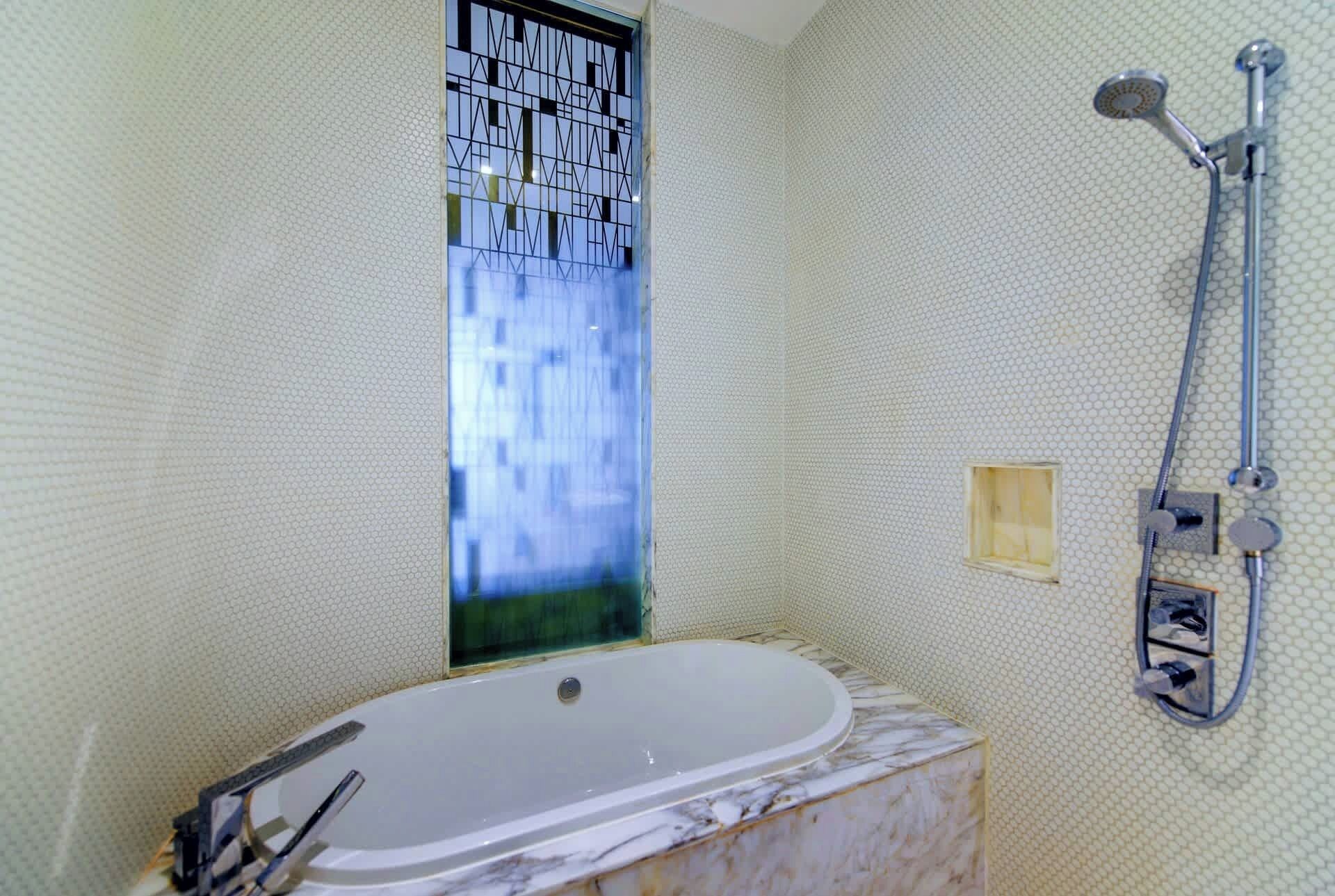 Ein Badezimmer mit einer großen Badewanne, einer Dusche und einem Fenster mit geometrischem Muster.