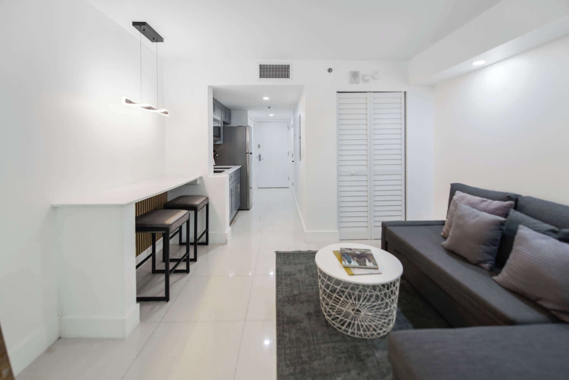 A modern living room with a sofa, a coffee table, and a kitchen area in the background.