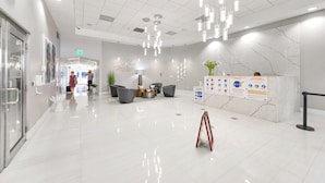 En moderne hotellobby med en ren, poleret gulv, et receptionsskrivebord med informationsplakater, og et siddeområde med stole og et lille bord.