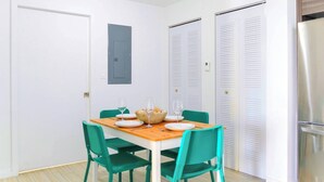 A dining area with a wooden table, green chairs, and a basket of bread. There are white doors and a small window with a blue shutter. - Free Parking - Near to Wynwood & Design District (Miami)