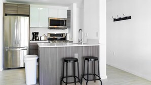 A modern kitchen with a stainless steel refrigerator, a microwave, a coffee maker, and a toaster. There are two black bar stools and a trash can. - Free Parking - Near to Wynwood & Design District (Miami)