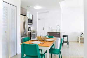 A modern kitchen with stainless steel appliances, a dining table with chairs, and a small stool.