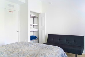 A bedroom with a bed, a black sofa, a wardrobe with a 'No Smoking' sign, and a shelving unit with folded towels. - Free Parking - Near to Wynwood & Design District (Miami)