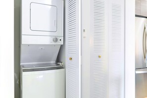 Eine kompakte Küche mit integriertem Waschtrockner, einem weißen Kühlschrank und einem Doppeltürenschrank mit goldener Griff.