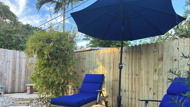 Deux fauteuils de jardin bleus, accompagnés d’un grand parasol, d’une clôture en bois et d’une terrasse carrelée.