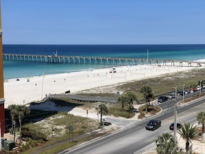 Uma praia com um cais, uma estrada com carros e um céu claro.