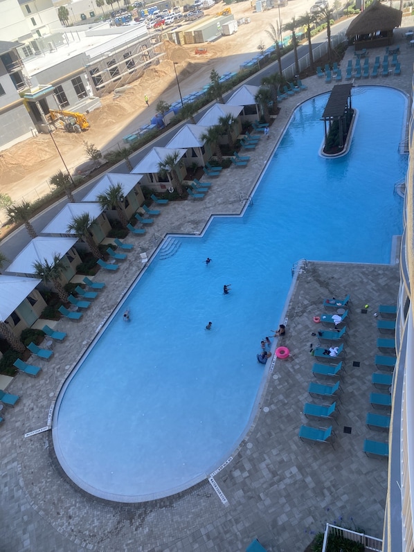 Uma grande piscina com várias pistas, rodeada por espreguiçadeiras e palmeiras.