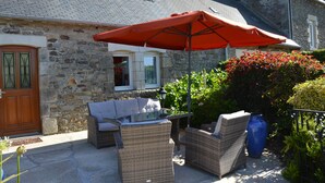 Un bâtiment en pierre avec une porte en bois, des meubles de jardin en osier et un parasol rouge.