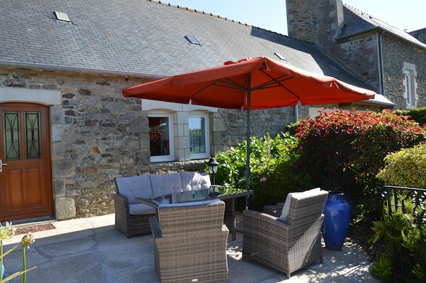 A stone building with a wooden door, outdoor wicker furniture, and a red umbrella.