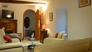 Un salon avec une télévision, des canapés, une lampe et un meuble en bois.