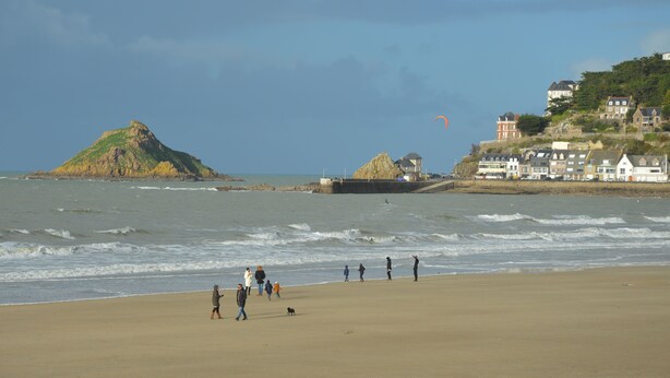 Une plage où l’on voit des gens se promener, avec un phare en arrière-plan.