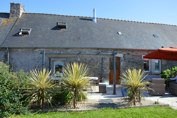 A stone building with a tiled roof, outdoor seating, and potted plants.