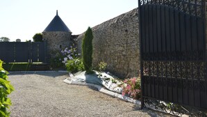 Un mur de pierres avec un portail en métal, une allée gravillonnée et, au fond, une structure à toit conique.