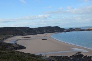 A coastal landscape with a sandy beach, rocky outcrops, and a clear sky.