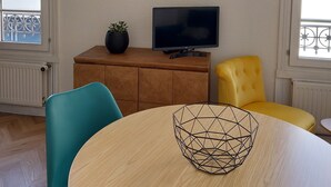 A modern living room with a round wooden table, a TV on a wooden cabinet, and a circular wall decoration with plants.
