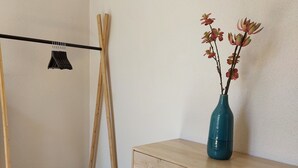 A room with a wooden herringbone floor, a wooden dresser with drawers, a blue vase with flowers, and a clothes drying rack.
