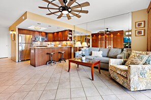 A spacious living area with a sofa, coffee table, and a kitchen area with wooden cabinets and a stainless steel refrigerator. - Hawaiian-inspired studio with ocean view (Lahaina)