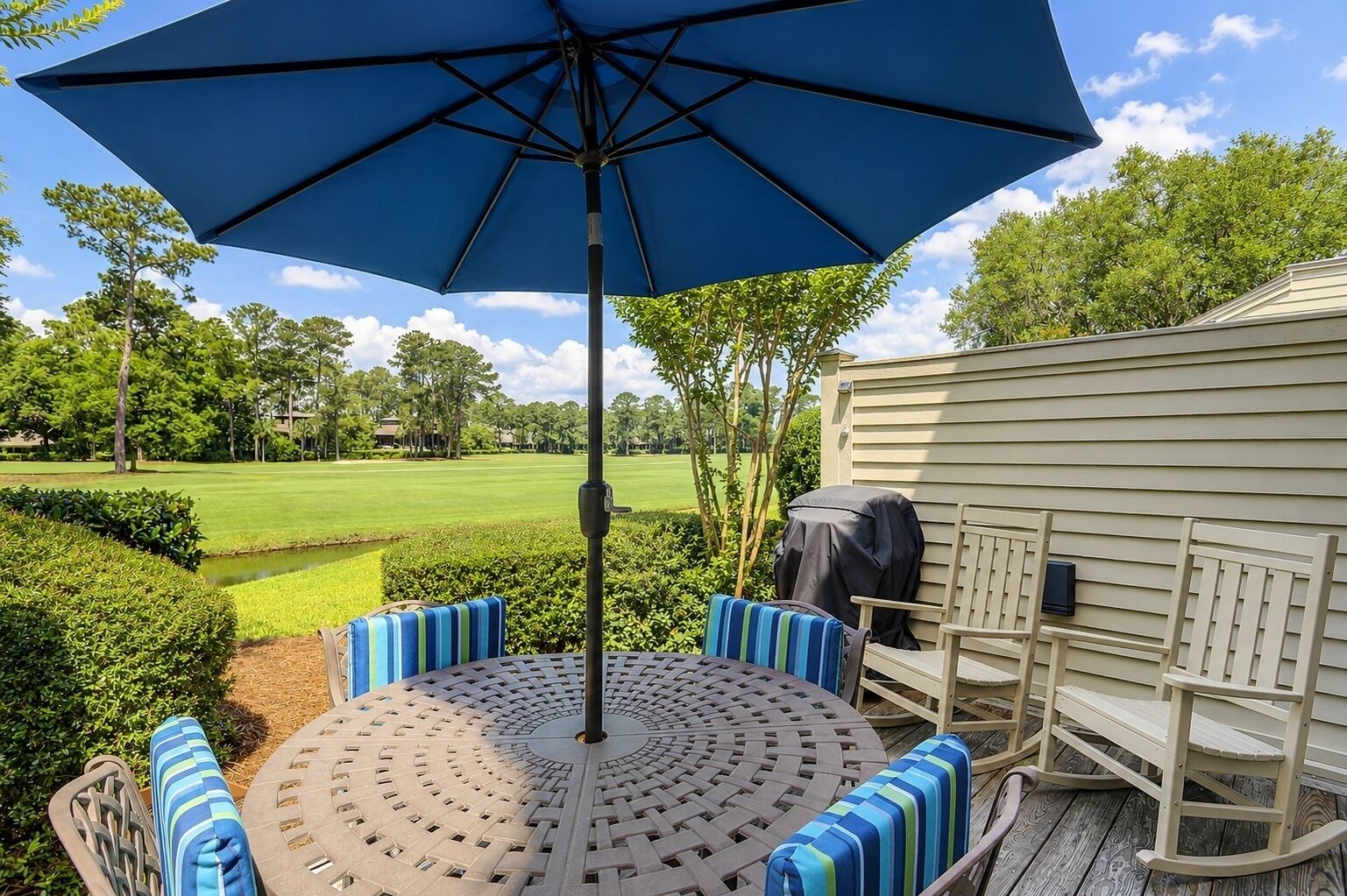 Eine Terrasse mit einem runden Tisch, blau gestreiften Kissen und einem großen, blauen Sonnenschirm.