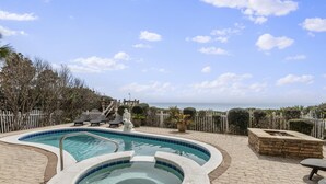 A swimming pool with a hot tub, lounge chairs, and a view of the ocean.