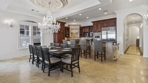 A spacious dining area with a large chandelier, a kitchen with modern appliances, and a hallway leading to another room.