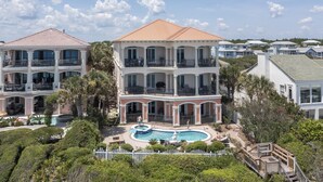 A large, multi-story residential building with a swimming pool, surrounded by lush greenery and a white picket fence.