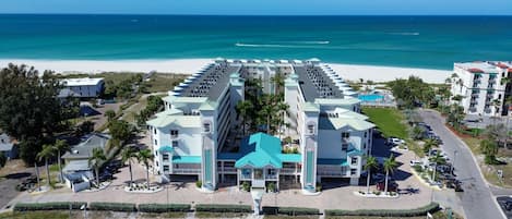 A beachfront hotel with a central atrium, multiple balconies, and a parking area.