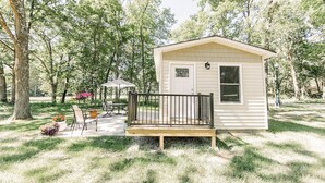 A small, single-story cabin with a porch, surrounded by trees and a patio area with outdoor furniture. - #3 Cabin at Red Oak Valley (Canaan Township)
