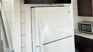 A kitchen with a white refrigerator, a microwave, and a flat-screen TV mounted above the fridge. - Tiny Home A at Red Oak Valley (Canaan Township)