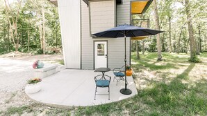 A modern house with a patio, two chairs, a table, and a large umbrella. - Tiny Home A at Red Oak Valley (Canaan Township)