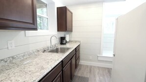 A kitchen with dark wooden cabinets, a granite countertop, a stainless steel sink, and a window providing natural light. - Tiny Home A at Red Oak Valley (Canaan Township)