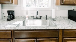 Una cocina con armarios de madera, un lavamanos de acero inoxidable, una cafetera y una ventana con vistas a árboles.