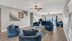 Ein großzügiges Wohnzimmer im modernen Stil, mit Deckenventilator, großem Fenster und blauem Sofa.