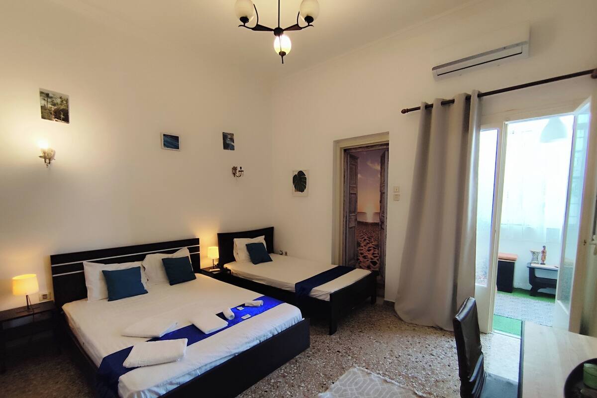 A hotel room with two beds, a chandelier, an air conditioning unit, and a view of the outside.