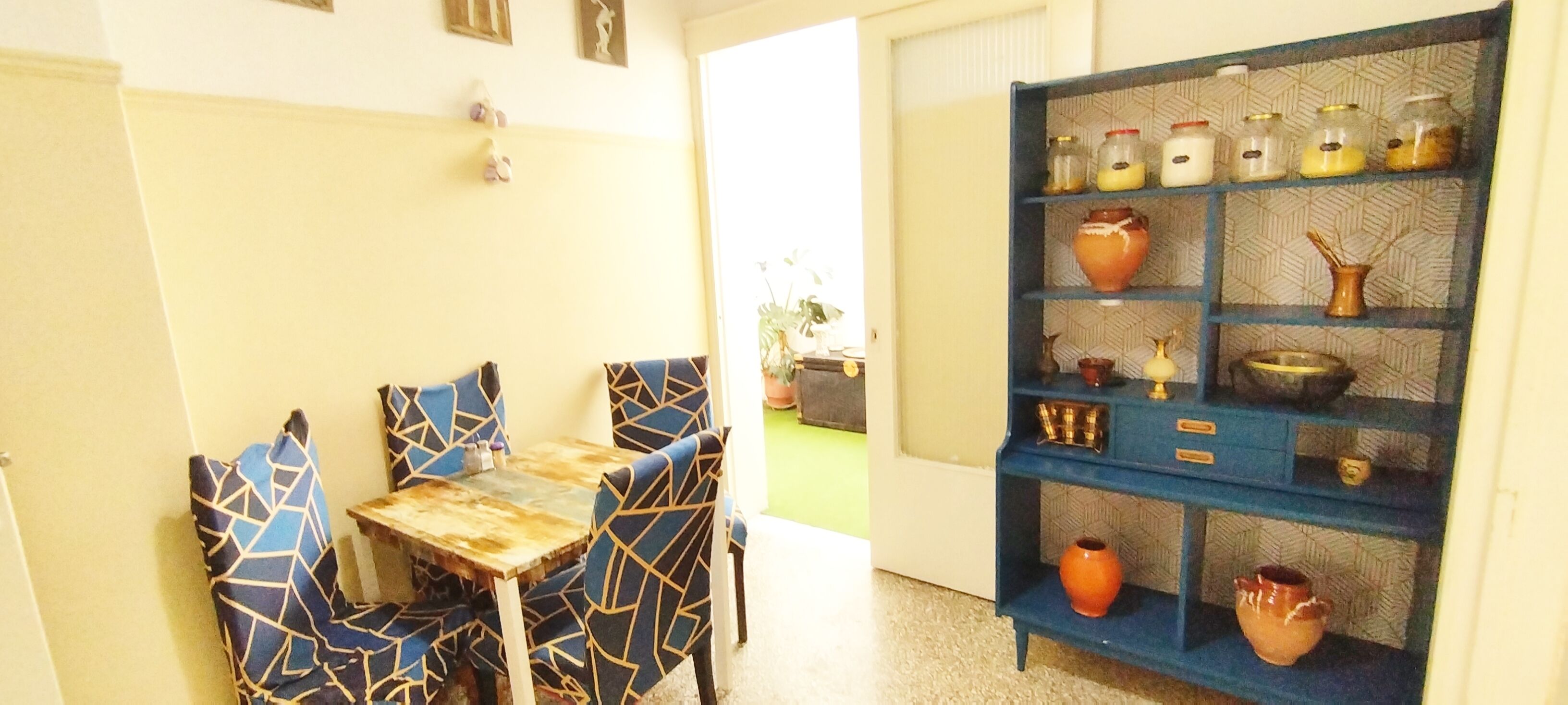Zona pranzo con tavolo e sedie, parete azzurra decorata con motivi e mensola con barattoli e oggetti decorativi.
