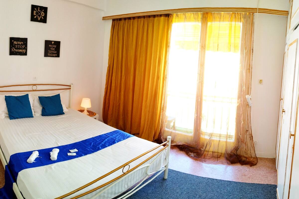 A neatly made bed with a blue accent, a bedside lamp, and a small table with a folded towel.