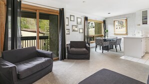 A modern living room with a sofa, armchair, dining area, and kitchen.