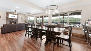 Un comedor amplio con una mesa larga y numerosas sillas, una chimenea y ventanas grandes que ofrecen vistas al exterior.