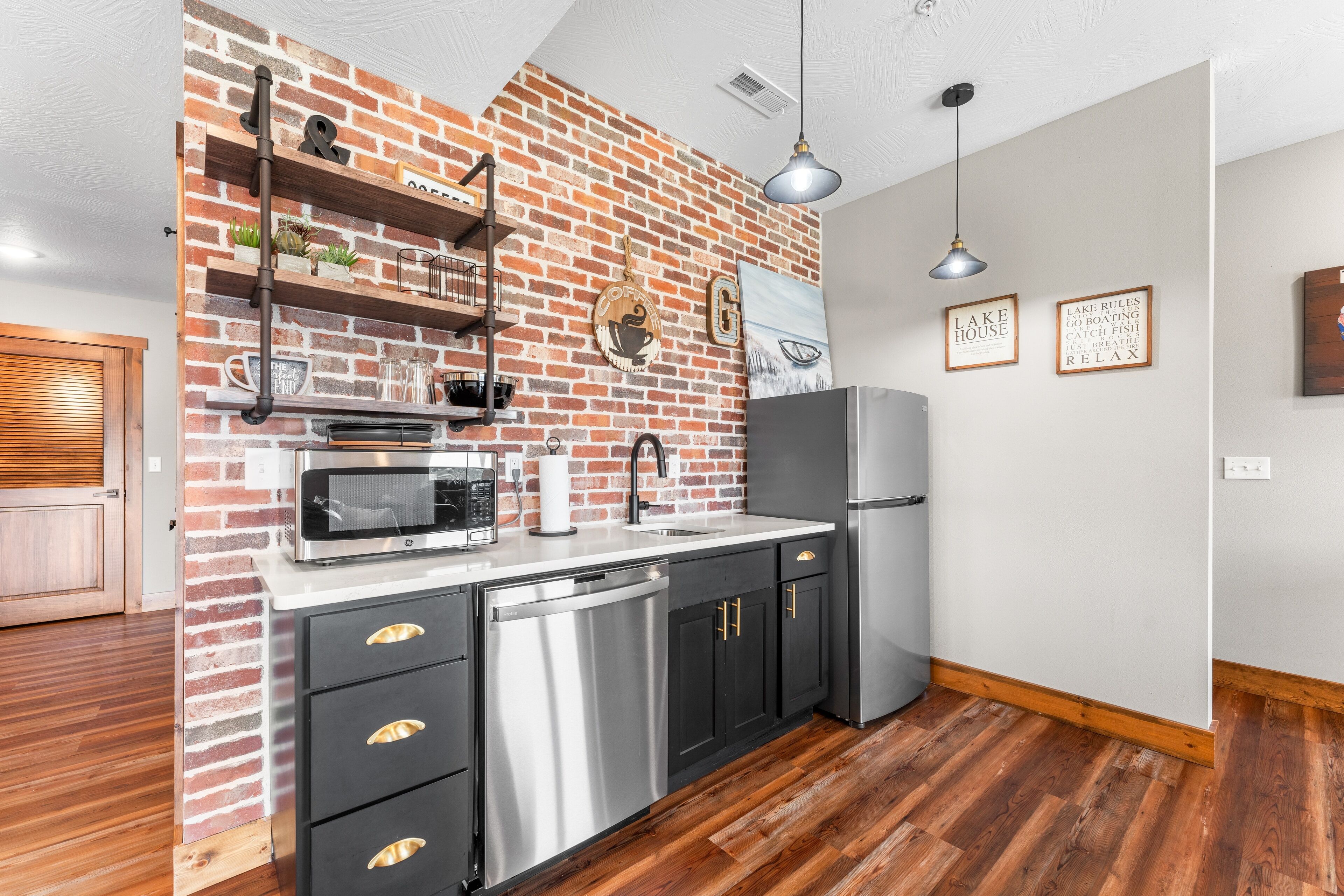 Una cocina con pared de ladrillo, electrodomésticos de acero inoxidable, piso de madera y puerta de madera.