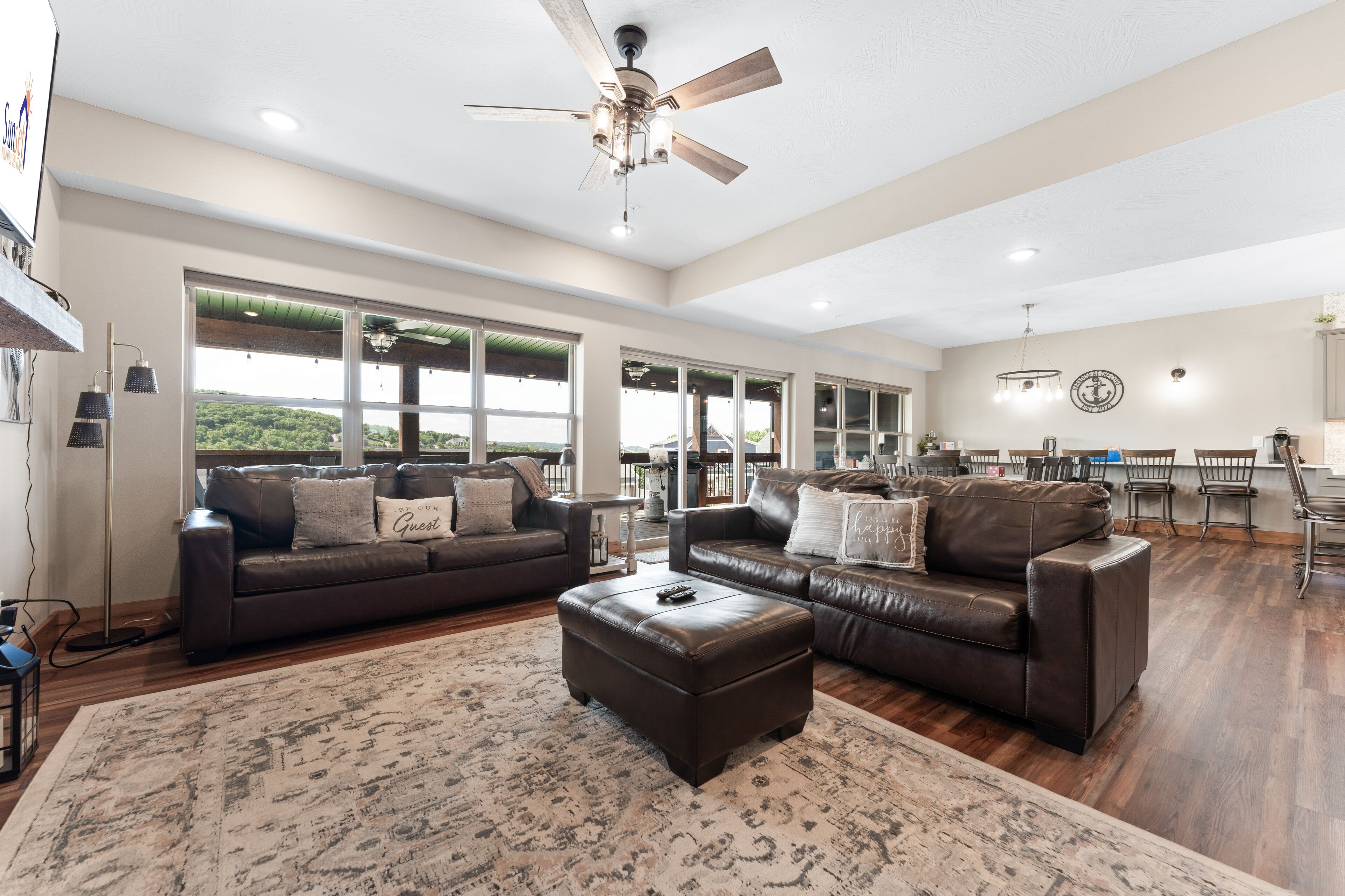 A spacious living room with leather sofas, a large rug, and a ceiling fan.